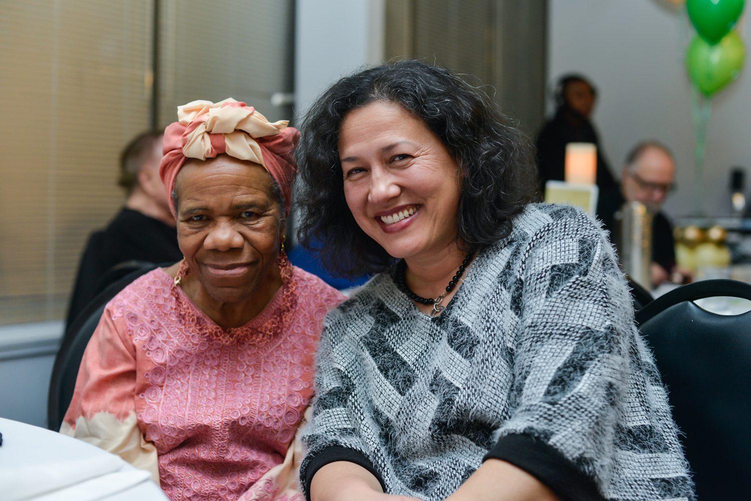 Two women sitting next to each other smiling.