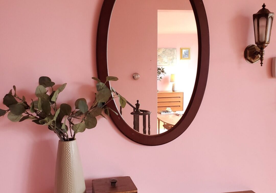 A mirror and vase on the wall of a room.